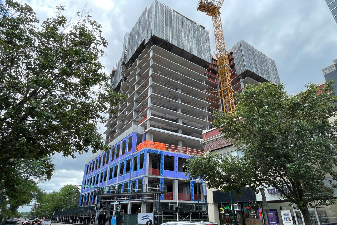 A cityscape featuring a building under construction, showcasing scaffolding and cranes against a clear blue sky.