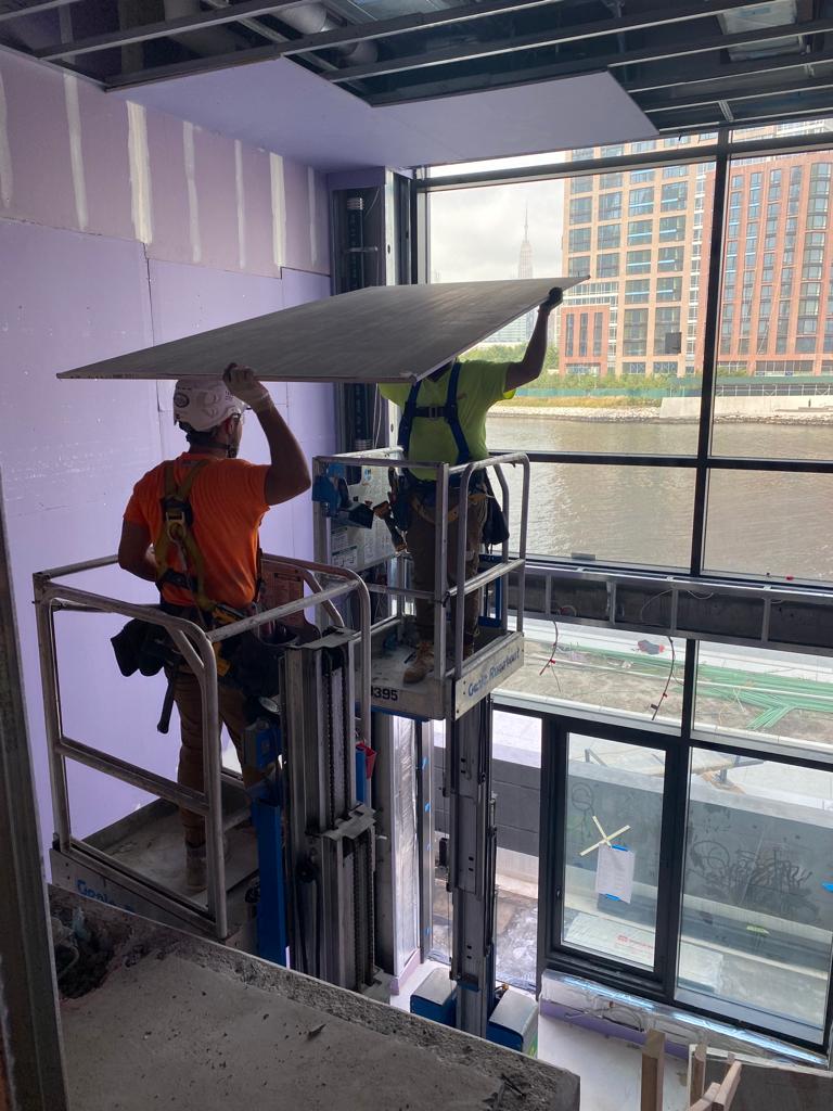 Two men diligently working together to install a large window in a building under construction.